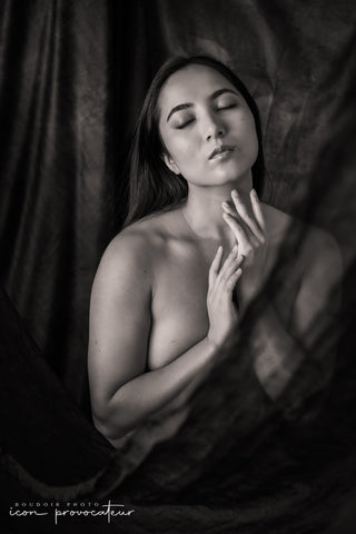 Black and white boudoir portrait of a woman with eyes closed, her hands softly touching her neck as sheer fabric frames her silhouette, a serene, elegant moment from the Allure session at Icon Provocateur, Montreal.