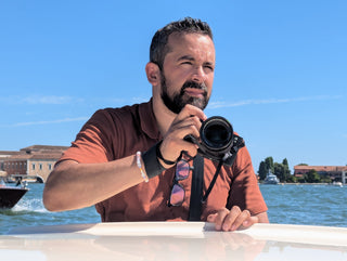 Napoleon holding a camera on a boat in Venice under bright daylight — a behind-the-scenes moment from Icon Provocateur’s creative journey.