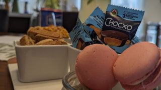 Close-up of a hospitality spread at Icon Provocateur, featuring pink macarons, candies, cookies, and Chocxo chocolates in a cozy kitchen setting.