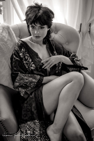 Black and white boudoir portrait of a woman seated in a tufted chair wearing a patterned robe, gazing confidently, elegant and editorial, part of the Icon experience at Icon Provocateur.