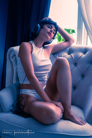 Stylized boudoir portrait of a woman in white crop top and underwear, lounging with headphones on a tufted chair, modern, intimate, and editorial, captured for the Icon package at Icon Provocateur.