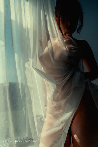 Female silhouette draped in sheer curtains, bathed in warm morning light, an ethereal and evocative nude portrait by Icon Provocateur, Montreal’s inclusive luxury boudoir studio.