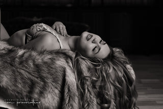 Woman reclining in lingerie over a faux fur throw, her head tilted back in soft ecstasy,  a sensual black-and-white boudoir portrait by Icon Provocateur, Montreal’s inclusive luxury studio.