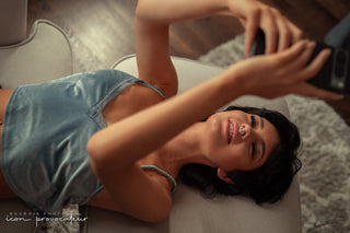 Woman laying back on a chaise, smiling softly as she takes a selfie — a playful and candid boudoir moment by Icon Provocateur, Montreal’s inclusive luxury studio.