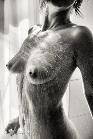 Close-up nude portrait of a woman under a streaming shower, water droplets catching the light, a raw and sensual boudoir image by Icon Provocateur, Montreal’s inclusive luxury studio.